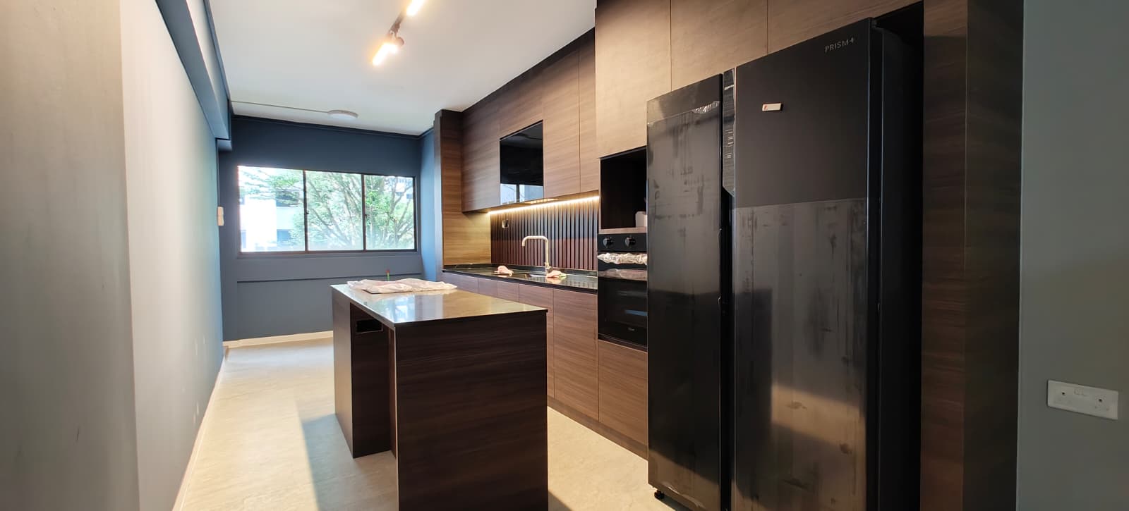 Kitchen wide view with island counter, black fridge, built-in oven and timber full-height cabinets